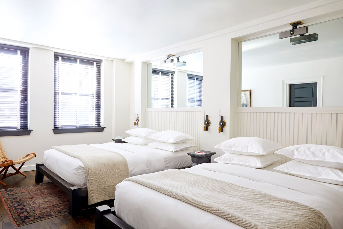 A hotel room with two beds, a wooden chair, a small table, and a large mirror.