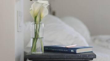 Una mesita de noche con un jarrón de flores blancas, un libro y una lámpara.