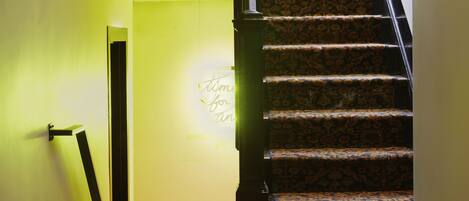 A staircase with a patterned carpet and a handrail, leading to a room with a green wall and a sign that reads "Watch Your Head".