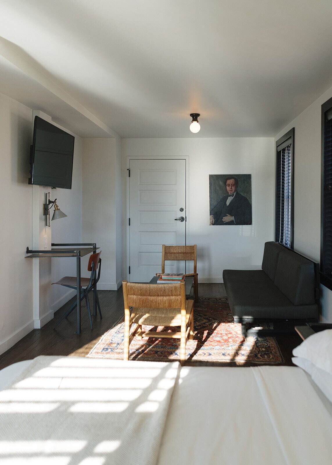 A room with a bed, a desk, a chair, a sofa, a television, and a painting on the wall.