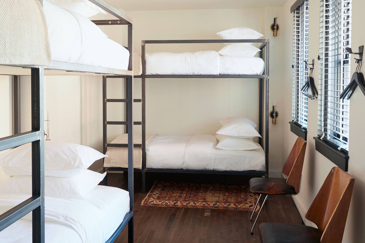 A bunk bed room with a wooden floor, a patterned rug, and a window with blinds.