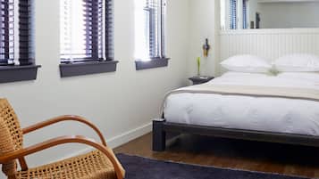 A bedroom with a bed, a chair, a nightstand, and a window with blinds.
