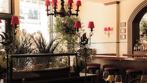 A restaurant interior with tables set for dining, a bar area, and a decorative plant arrangement.