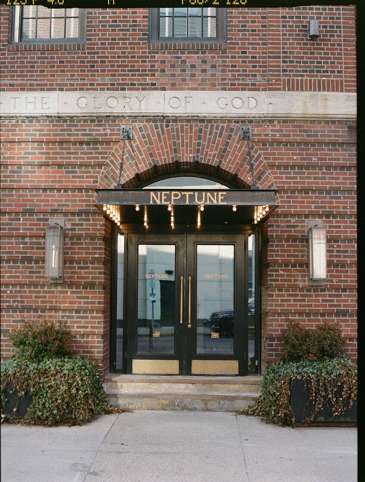 A brick building with a sign reading 'The Glory of God' and 'NEPTUNE' above the entrance.