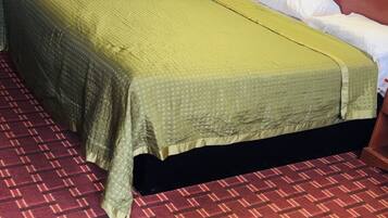 A single bed with a green bedspread and white pillows in a room with a red carpet and a wooden headboard.