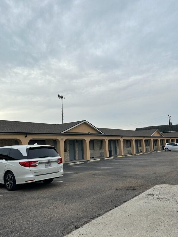 A motel with a row of rooms, a parking lot, and a white car parked in front.