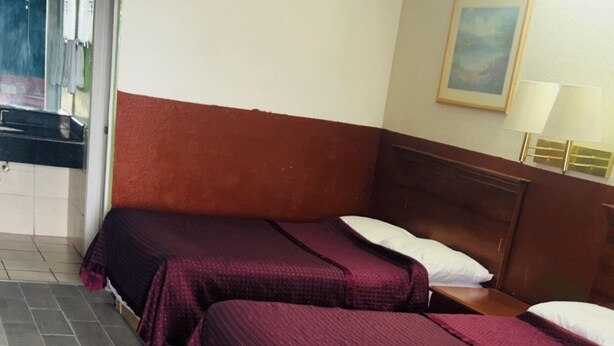 A hotel room with two beds, a wooden headboard, a painting on the wall, and a tiled floor. - Executive Inn (Robstown)