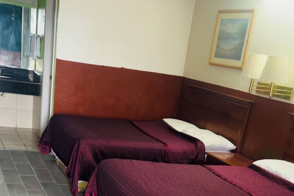 A hotel room with two beds, a wooden headboard, a painting on the wall, and a tiled floor.