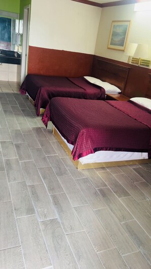 A hotel room with two beds, a wooden headboard, a painting on the wall, and a tiled floor.