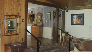 Uma sala de estar ampla com teto alto, vigas de madeira, uma escadaria de pedra e vista para uma área de cozinha.