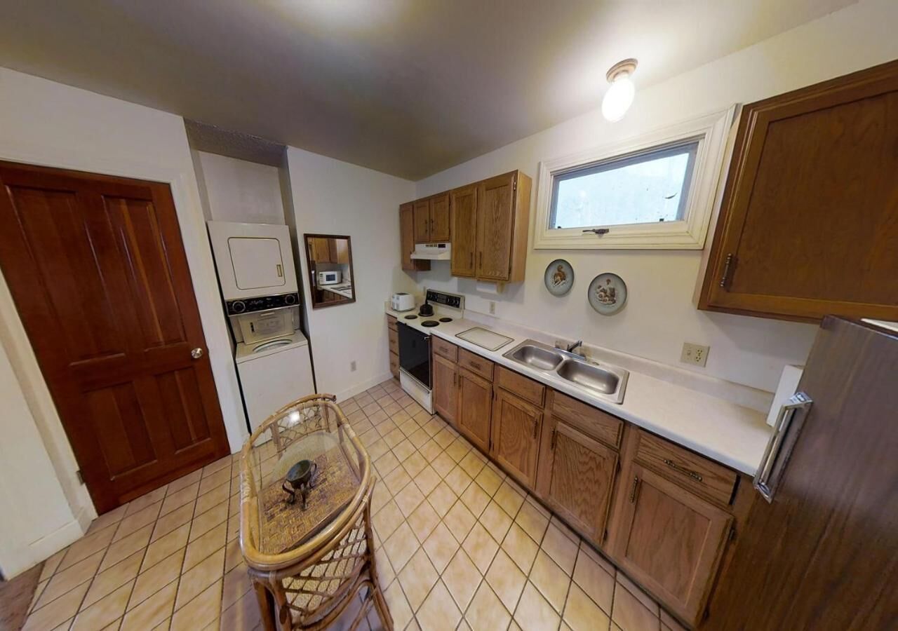 A compact kitchen with wooden cabinets, a built-in microwave, a stove, and a sink. There's a dining table with chairs and a window above the sink.