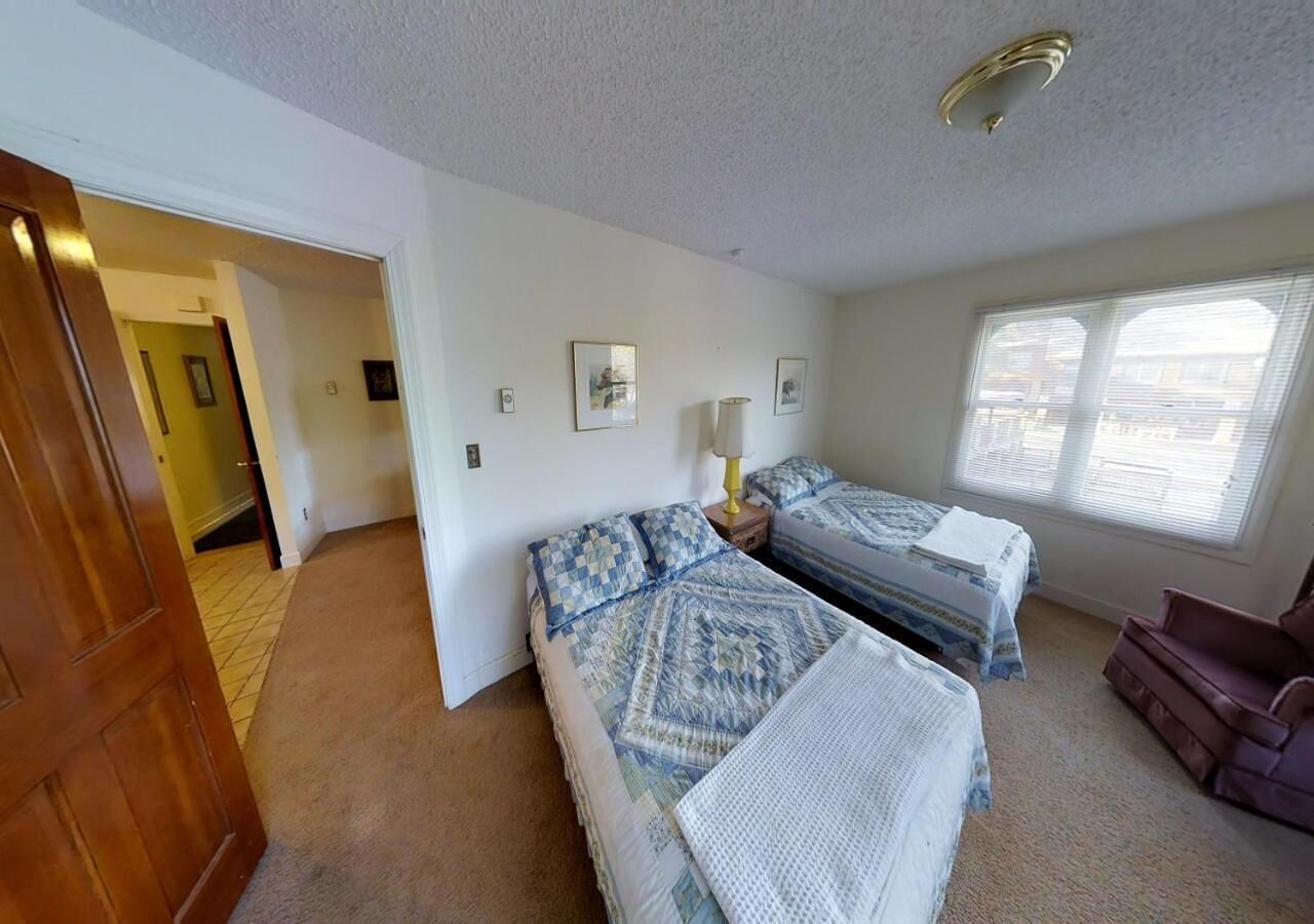 A bedroom with two beds, a window, and a door leading to another room.