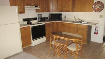 A compact kitchen with wooden cabinets, a stove, microwave, and a dining table with chairs.