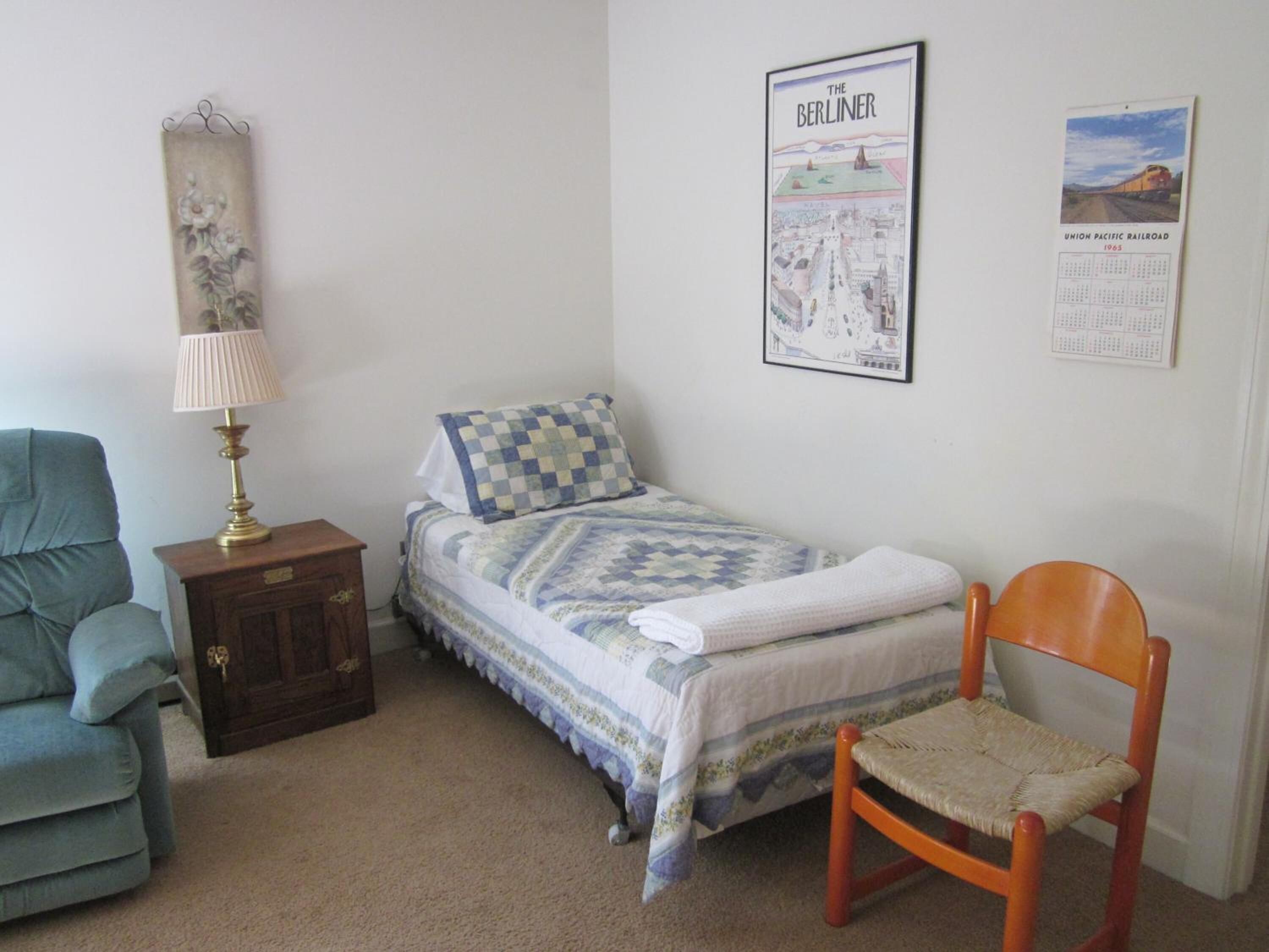 A bedroom with a bed, a chair, a nightstand, a lamp, and two posters on the wall.