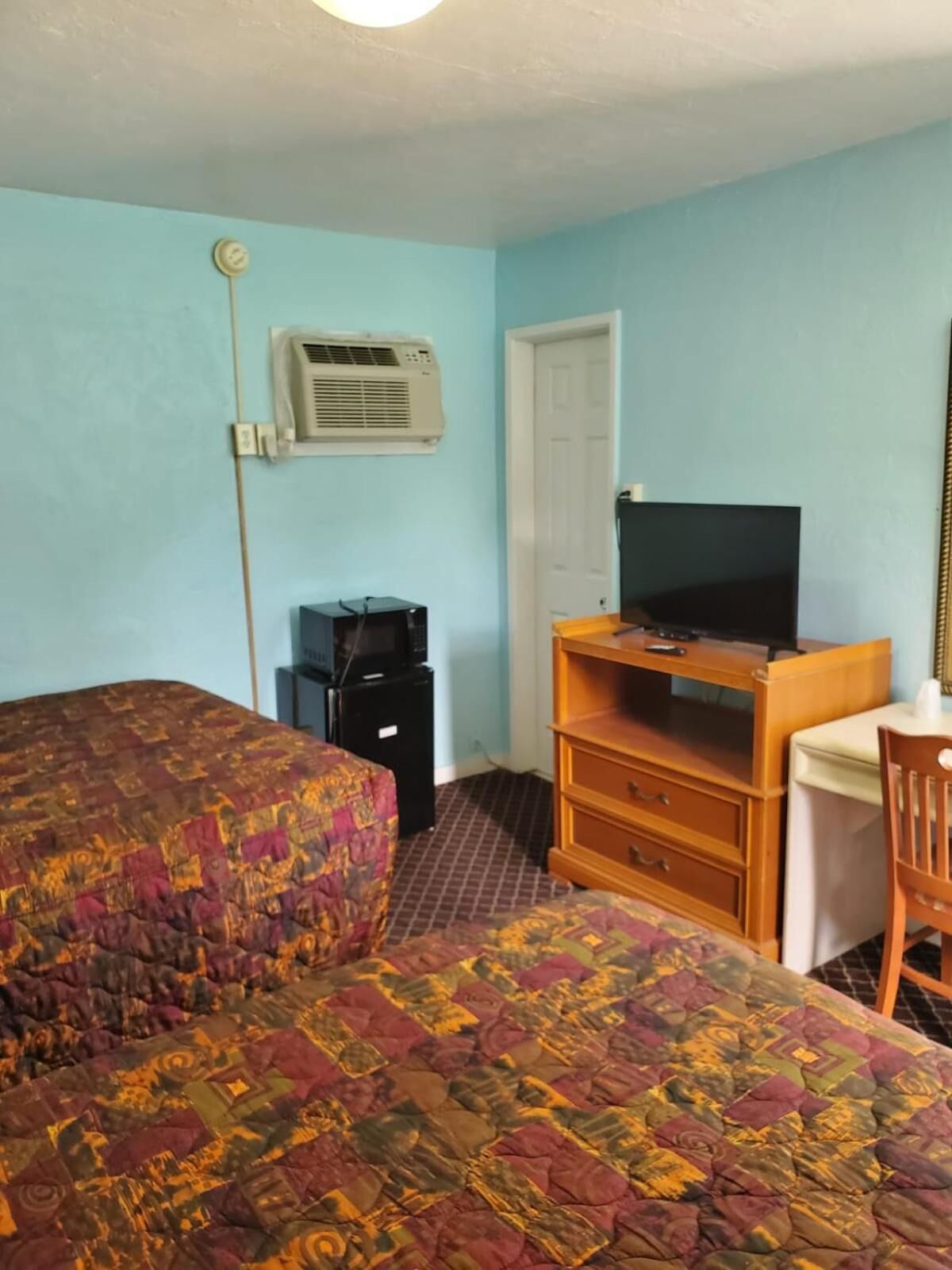 A room with two beds, a desk with a computer, an air conditioning unit, and a door.