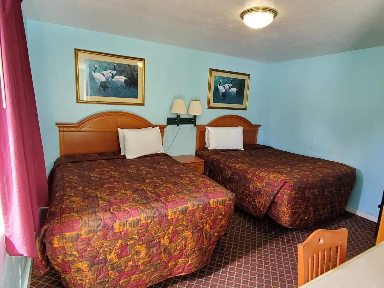A hotel room with two beds, each with a patterned bedspread, a nightstand with lamps, and two framed pictures on the wall.