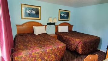 A hotel room with two beds, each with a patterned bedspread, a nightstand with lamps, and two framed pictures on the wall.
