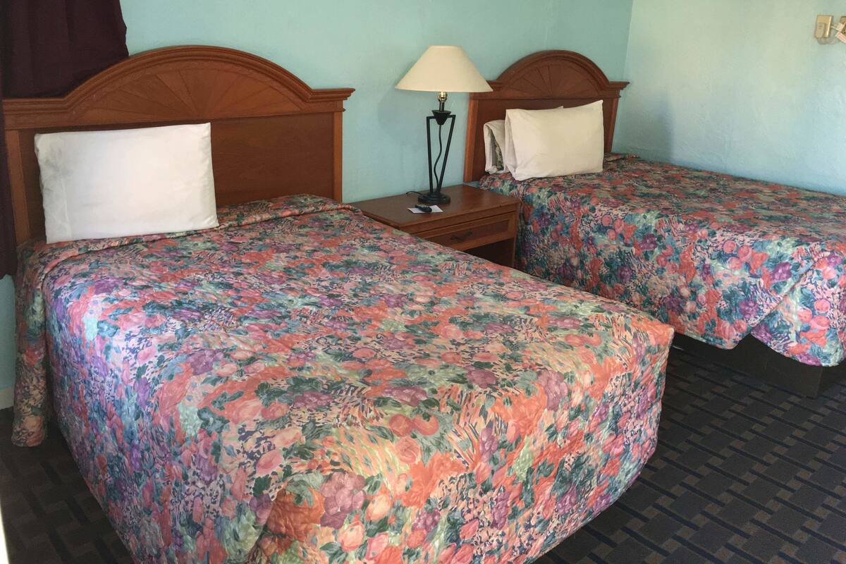 A room with two beds, each with floral bedspreads, a nightstand with a lamp, and a wooden headboard.