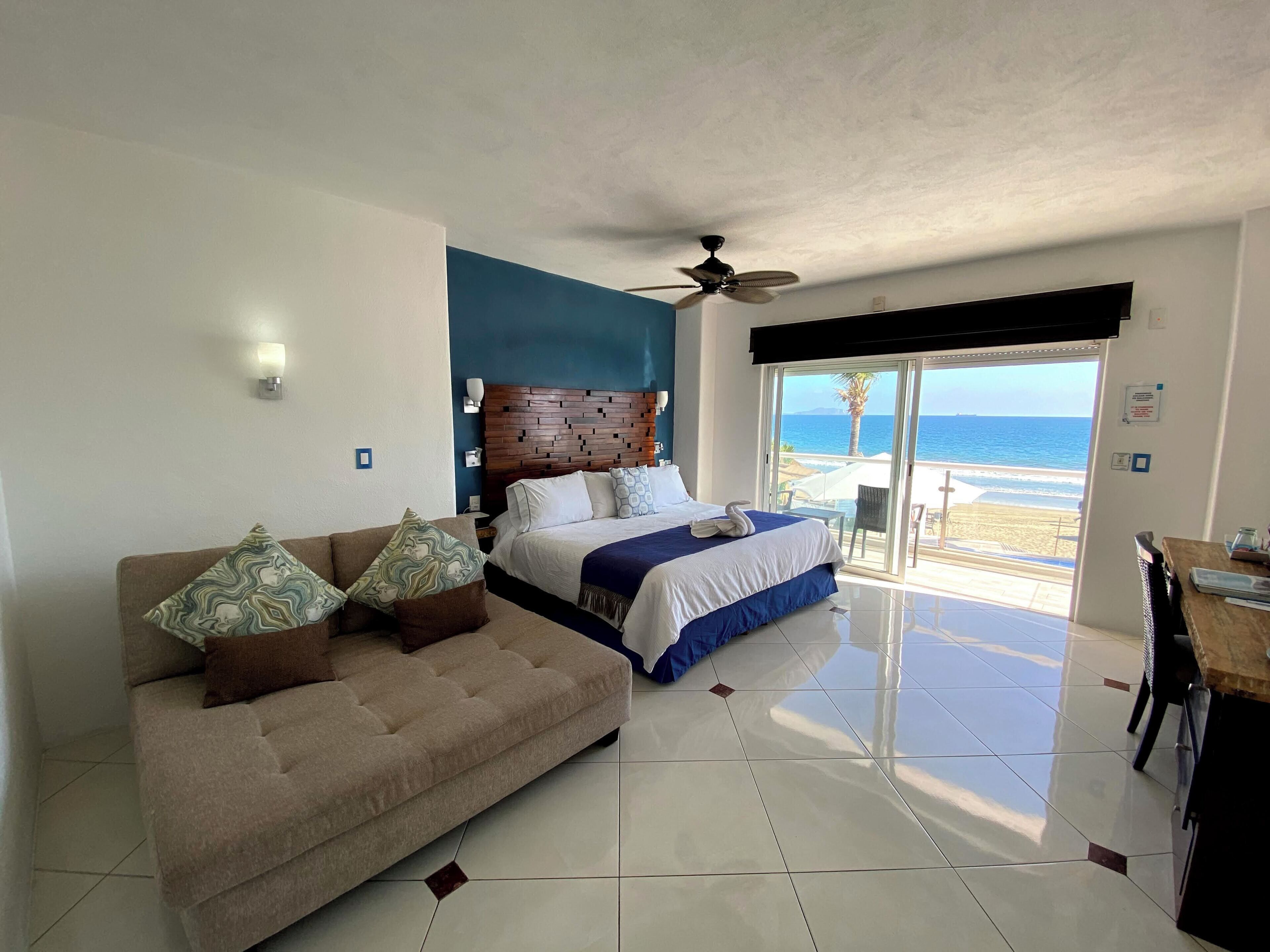 Une chambre avec un lit, un canapé, un ventilateur de plafond et vue sur la plage.