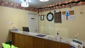 Zona de recepción de un hotel con mostrador de mármol, un reloj y varios carteles informativos.