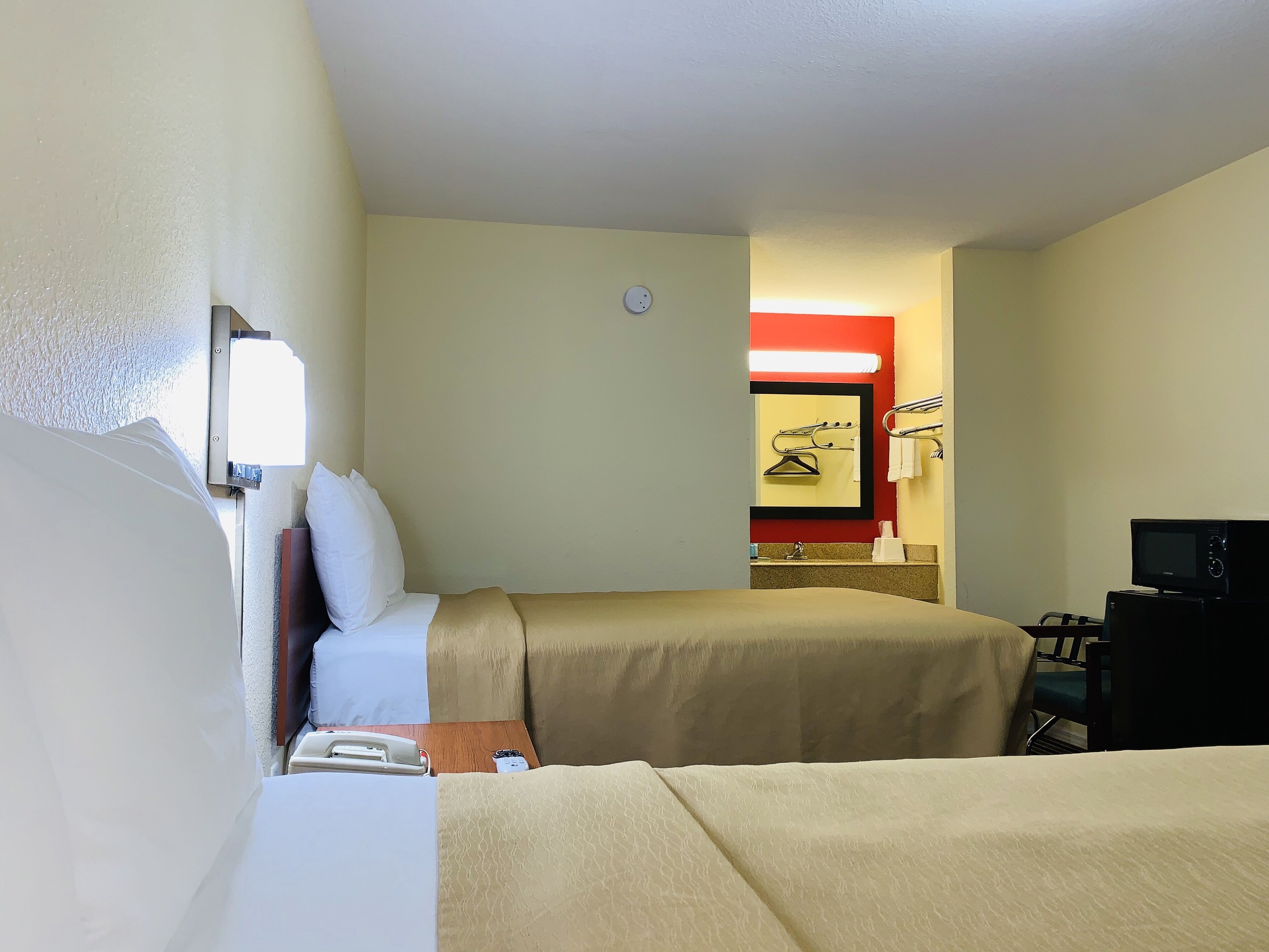 Une chambre d’hôtel avec deux lits, un bureau, un miroir et une télévision.