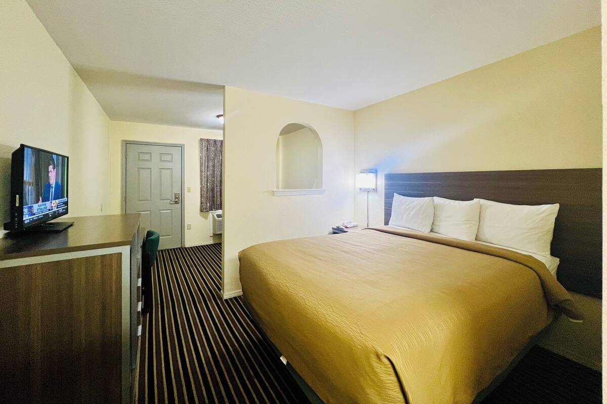 Una habitación de hotel con cama, escritorio, televisión y puerta.