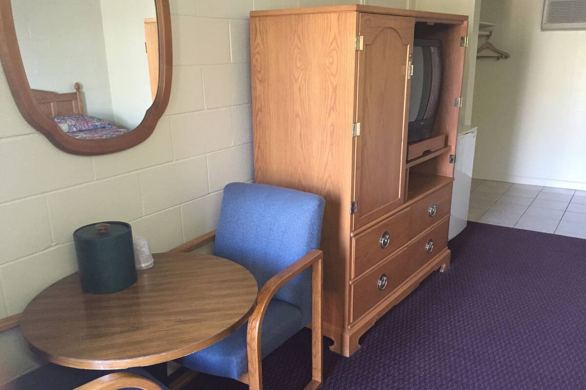 A room with a wooden cabinet, a blue chair, a small wooden table, and a mirror on the wall.