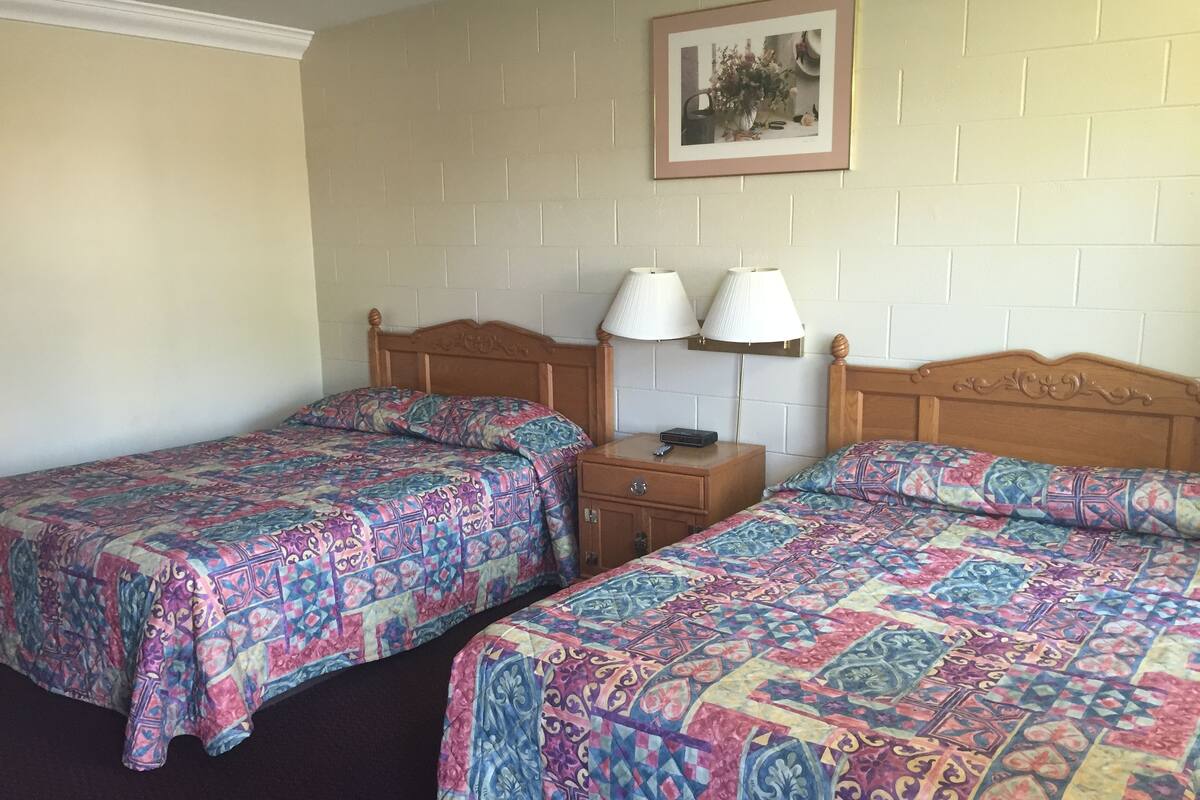 A room with two beds, each with a patterned bedspread, a nightstand with a lamp, and a picture on the wall.