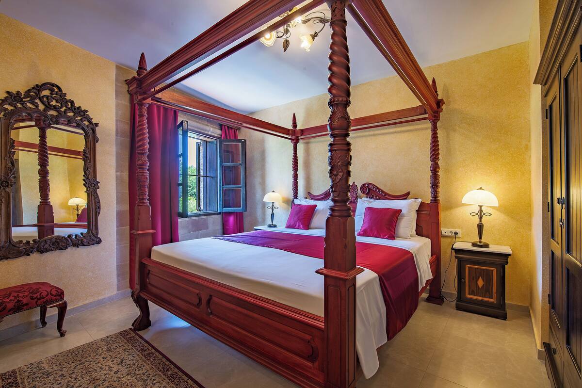 A four-poster bed with a canopy, a large ornate mirror, and a small bedside table with a lamp.