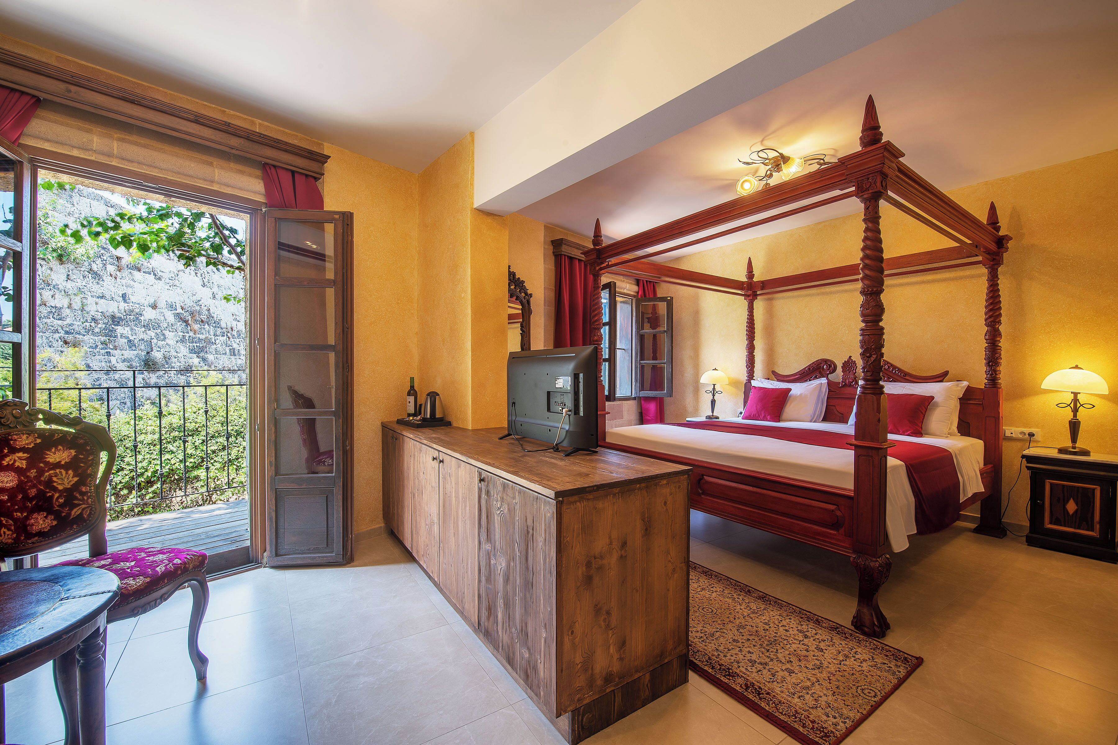 Un dormitorio con cama con dosel, un escritorio de madera, un televisor y vistas al exterior.