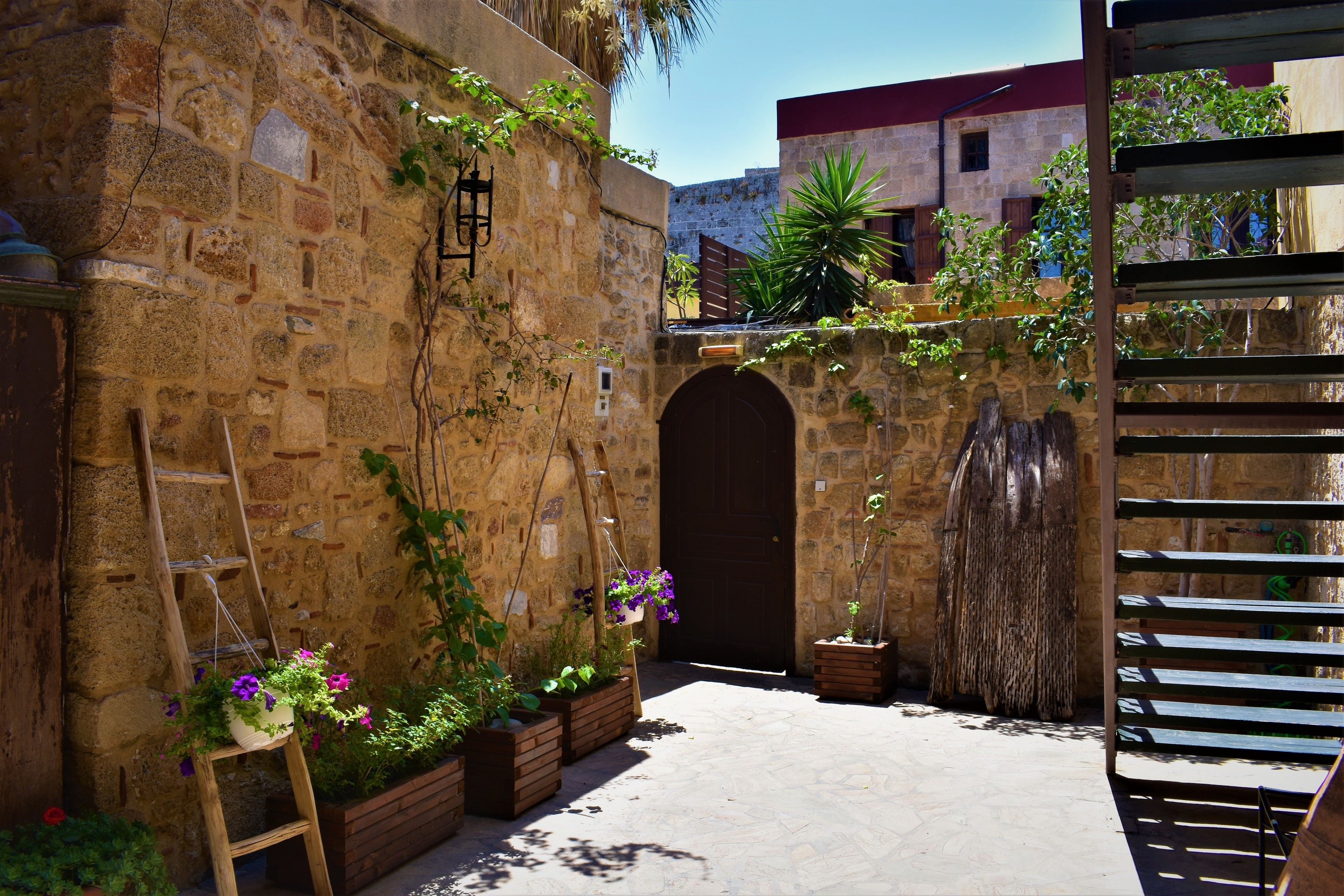 A courtyard with stone walls, wooden benches, and potted plants.