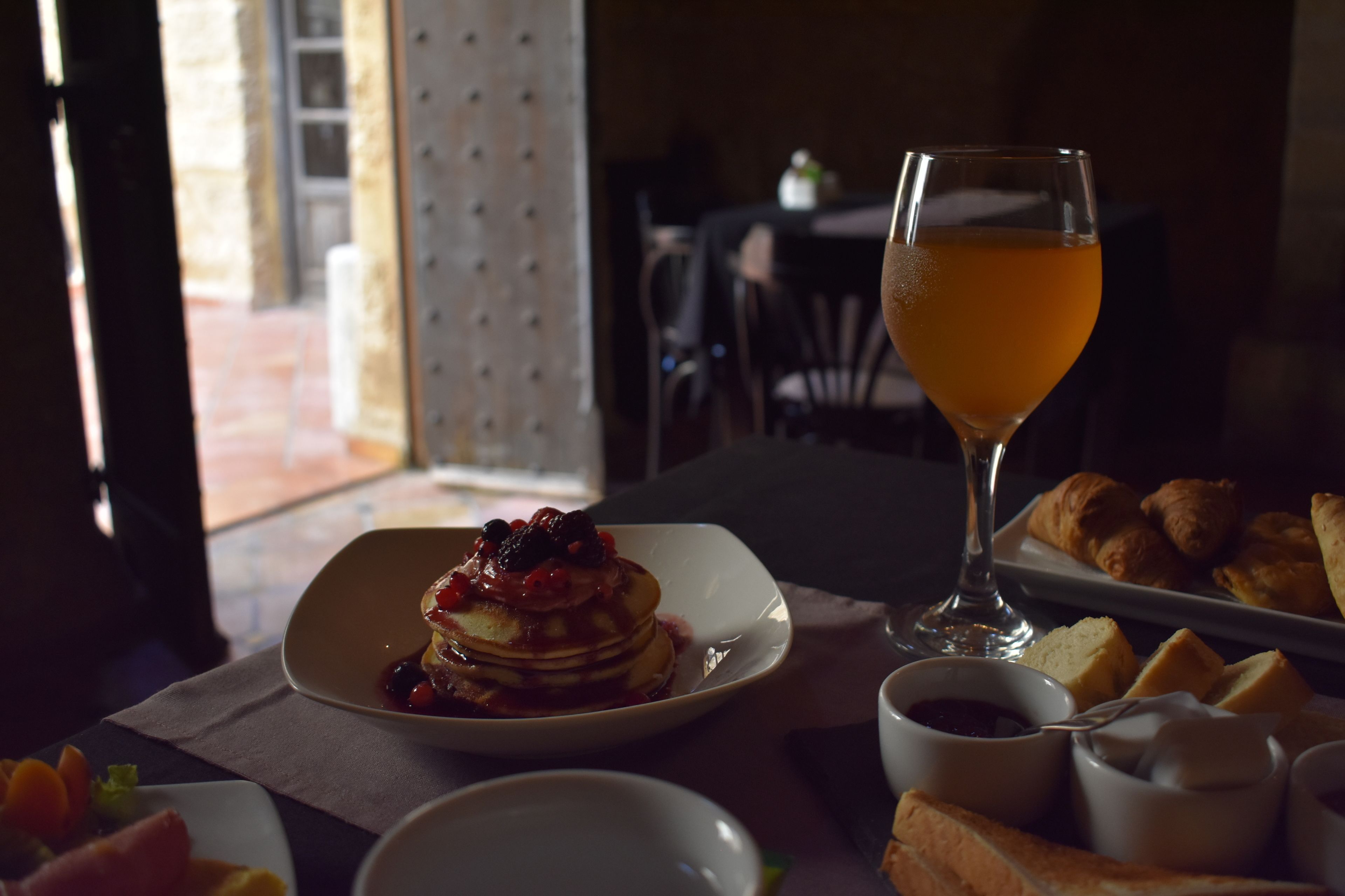 A breakfast setting with pancakes, croissants, and a glass of orange juice.