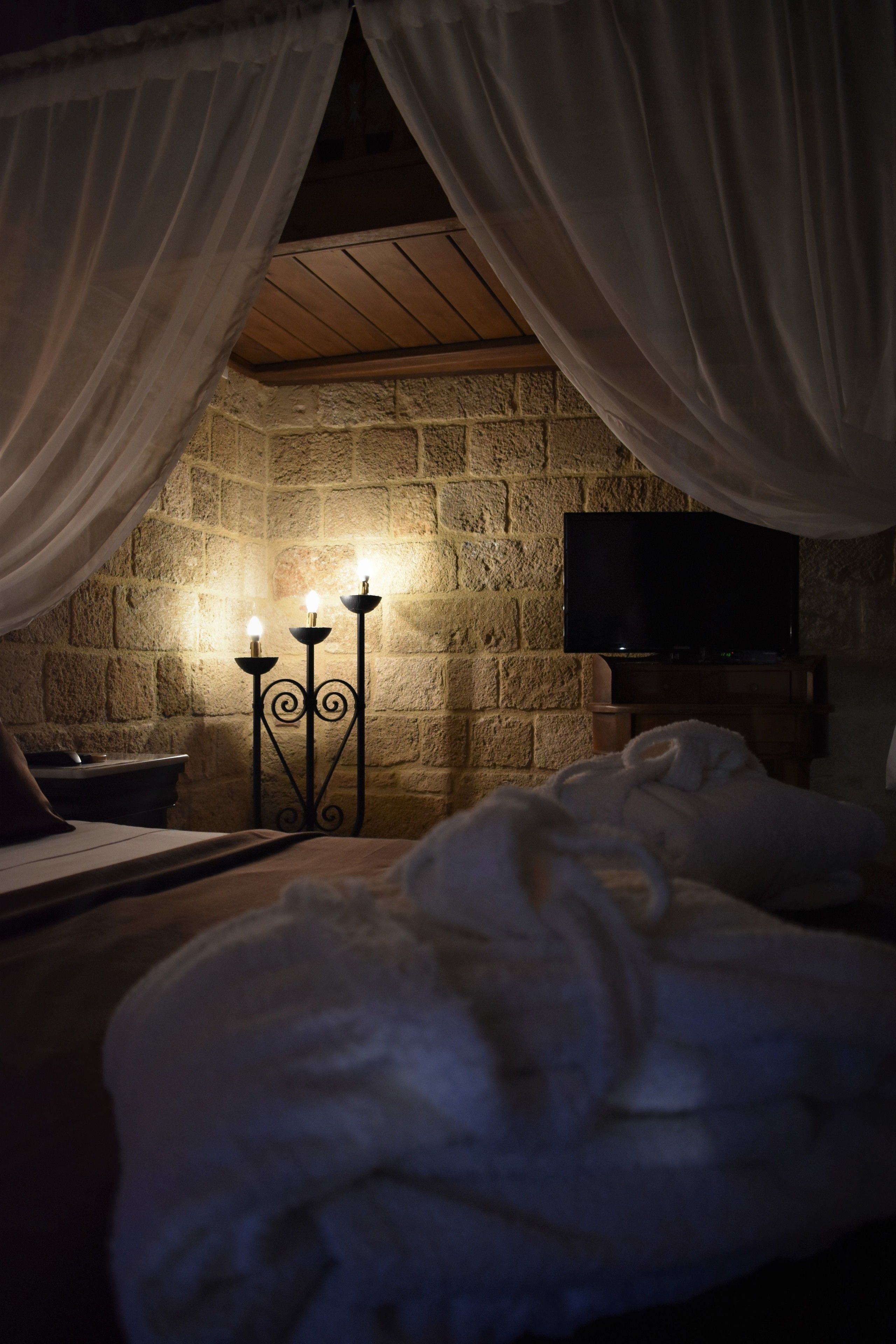 A cozy bedroom with a stone wall, a flat-screen TV, and a bed with white bedding.