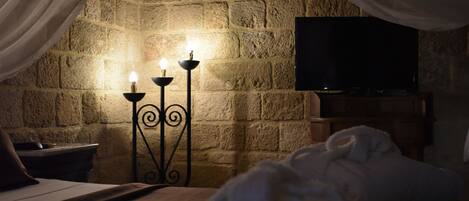 A cozy bedroom with a stone wall, a flat-screen TV, and a bed with white bedding.
