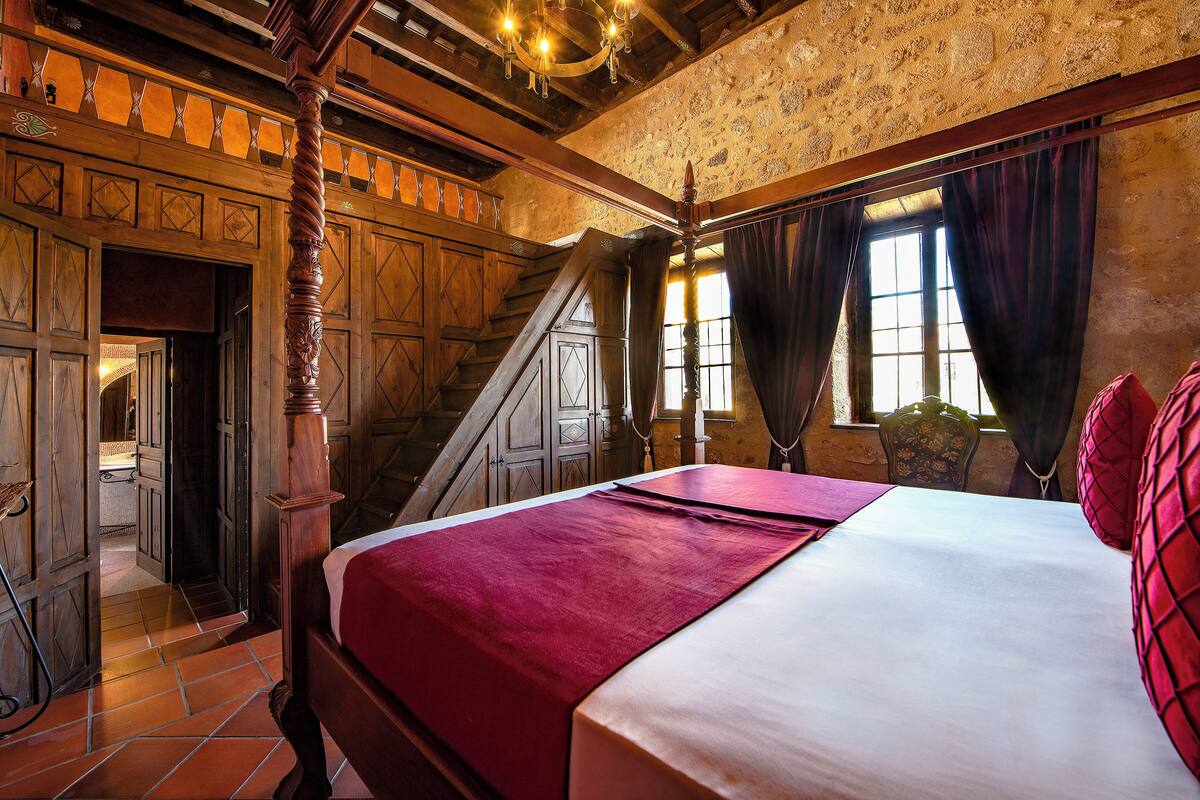 A traditional room with a wooden staircase, a bed with a red and white bedspread, and a chandelier.