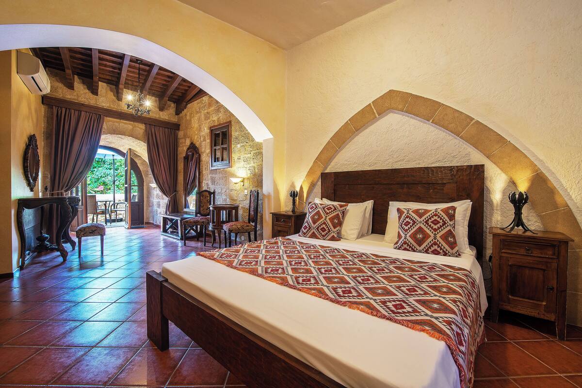 A bedroom with a large bed, wooden headboard, and an arched stone wall.