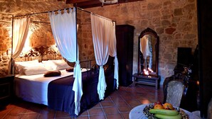 Un dormitorio de paredes de piedra con cama con dosel, un espejo y un frutero en el suelo.
