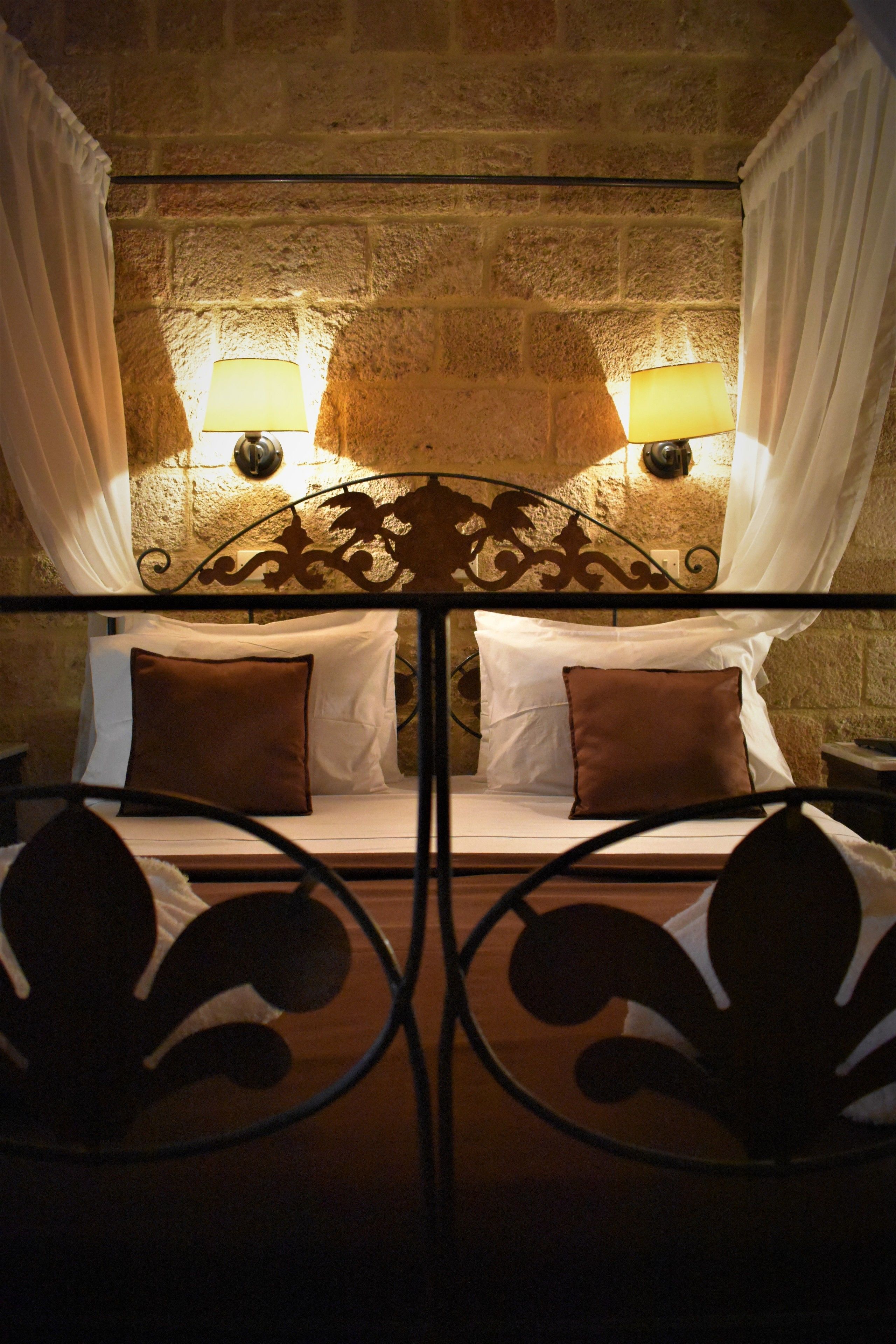 A bed with a metal headboard, two bedside lamps, and white curtains.