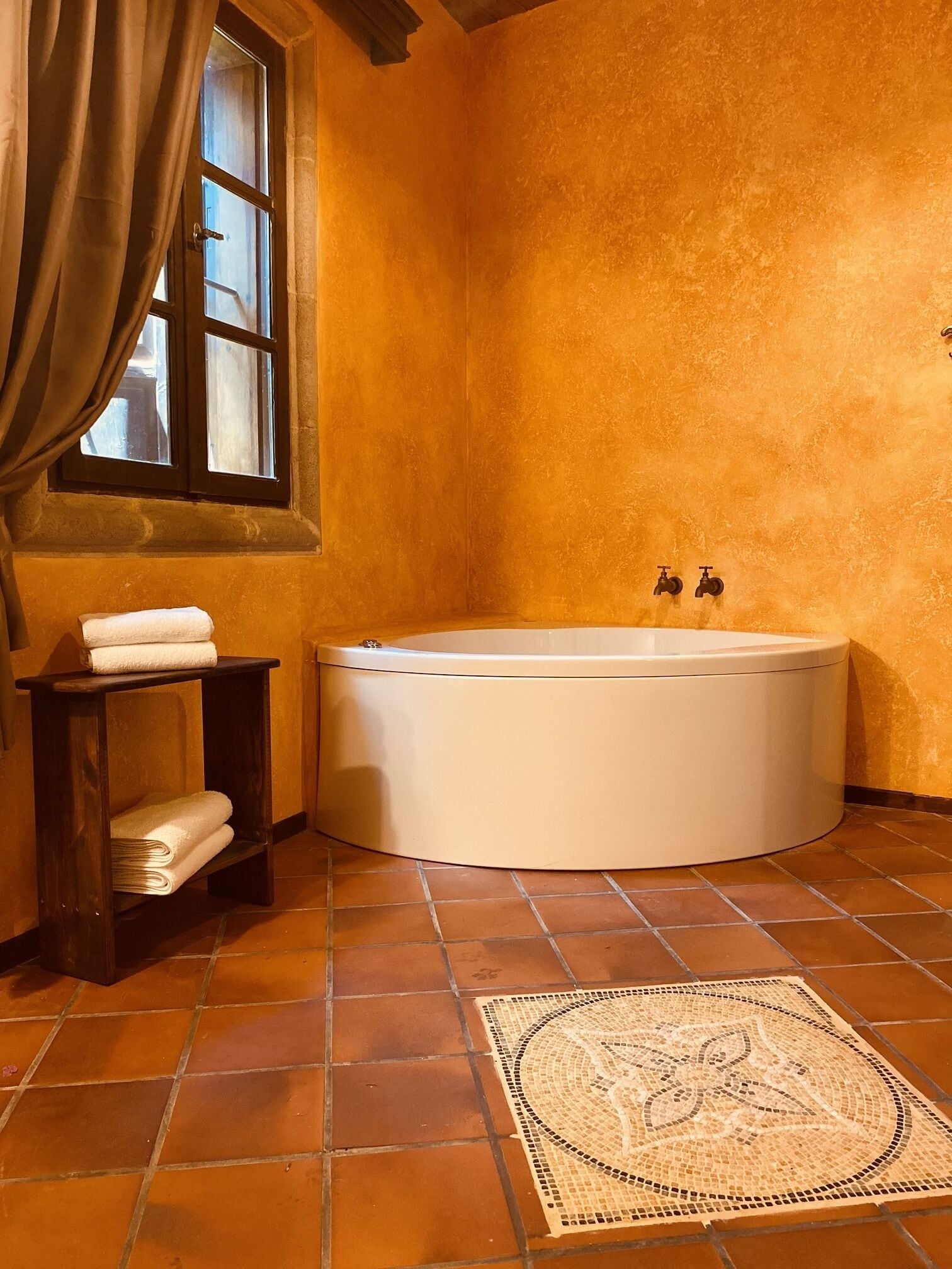 Un baño con bañera, una ventana con cortinas, un perchero y suelo de baldosas.