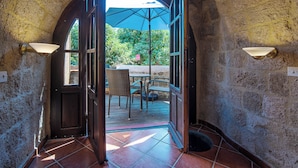 Un arco de entrada da a un patio exterior con una mesa y sillas, rodeado de muros de piedra y un piso de baldosas.