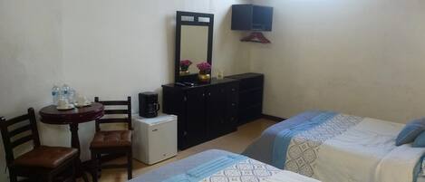 Une petite pièce simple, avec deux lits, un bureau, une chaise et une commode.