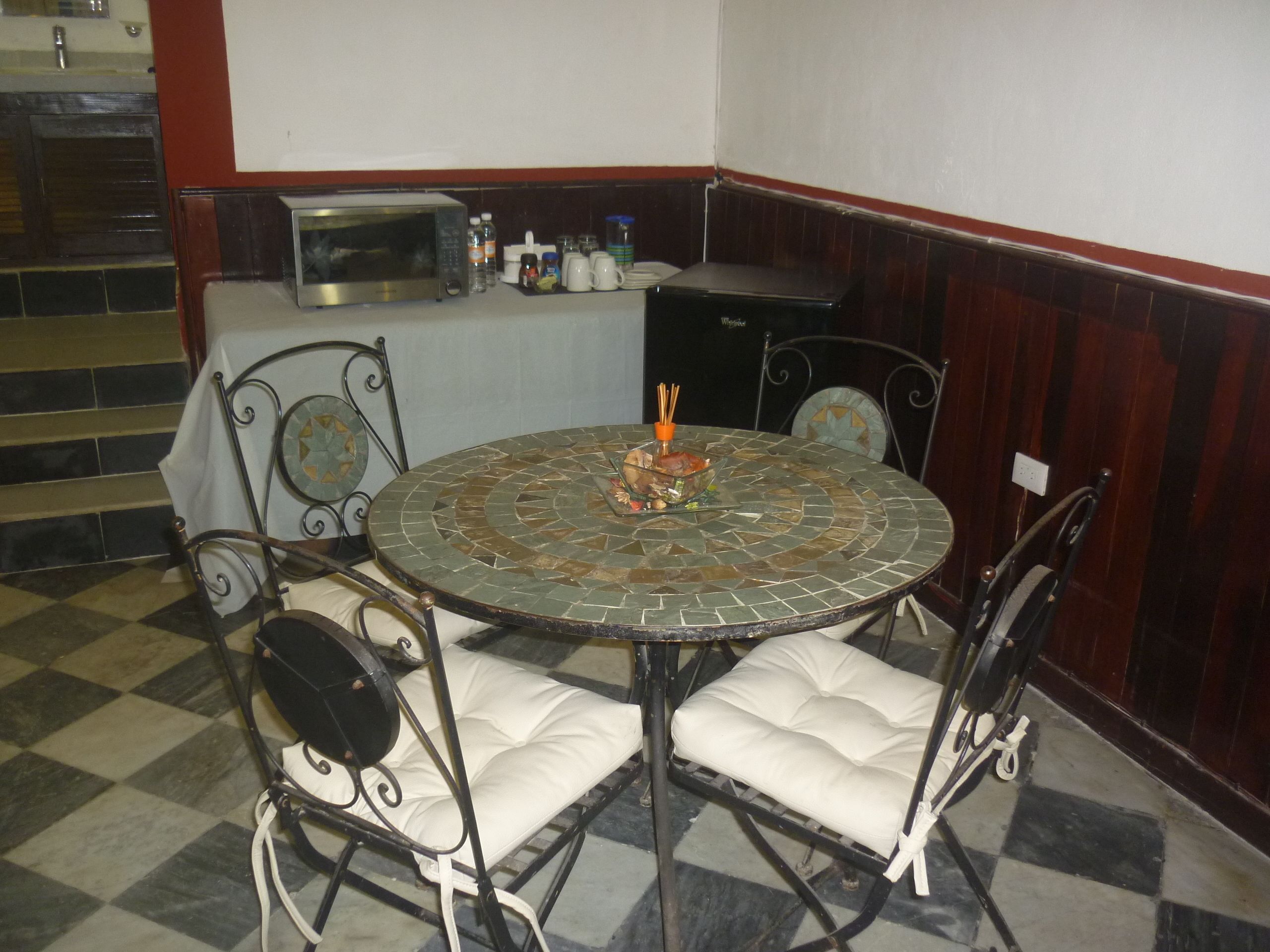 Un rincón comedor con una mesa de mosaico, sillas acolchadas, microondas y una pequeña encimera de cocina.