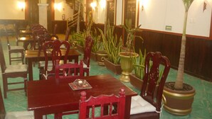 Un comedor con mesas y sillas de madera, plantas en macetas y una escalera que sube a un nivel superior.