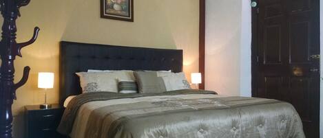 Una camera da letto con un letto grande, due comodini con lampade, una testiera scura, un quadro incorniciato appeso al muro e una porta in legno scuro.