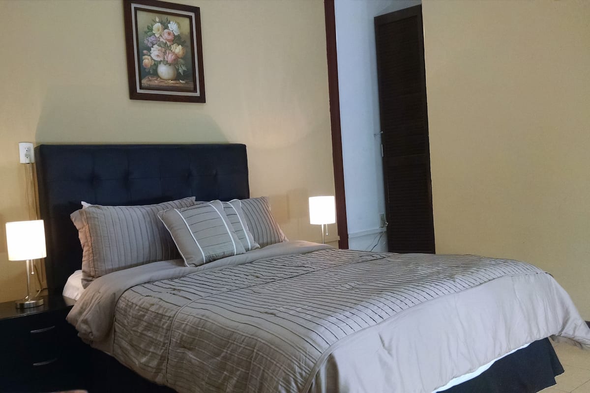 A neatly made bed with a dark headboard, two bedside tables with lamps, and a framed floral artwork above the bed.