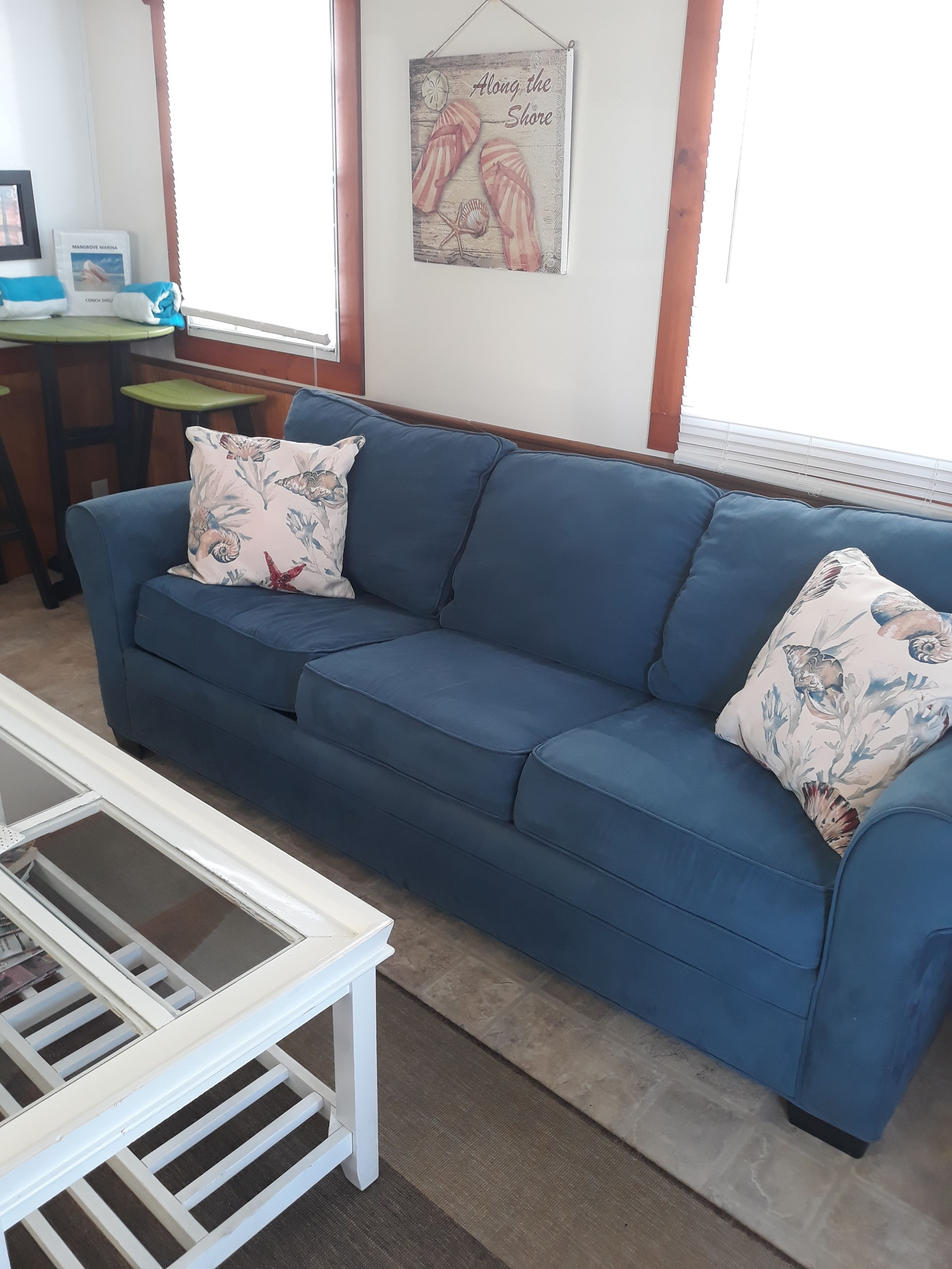 A blue sofa with floral cushions, a white coffee table, and a framed picture of flip-flops on the wall.
