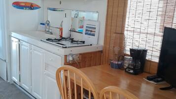 Une cuisine compacte avec des meubles blancs, un four à micro-ondes, une cuisinière à gaz et une table à manger avec deux chaises en bois.