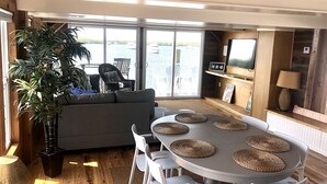 A modern living room with a large window, a grey sofa, a dining table with woven placemats, and a potted plant. - Mangrove Marina and Resort Aqualodge Houseboats (Tavernier)