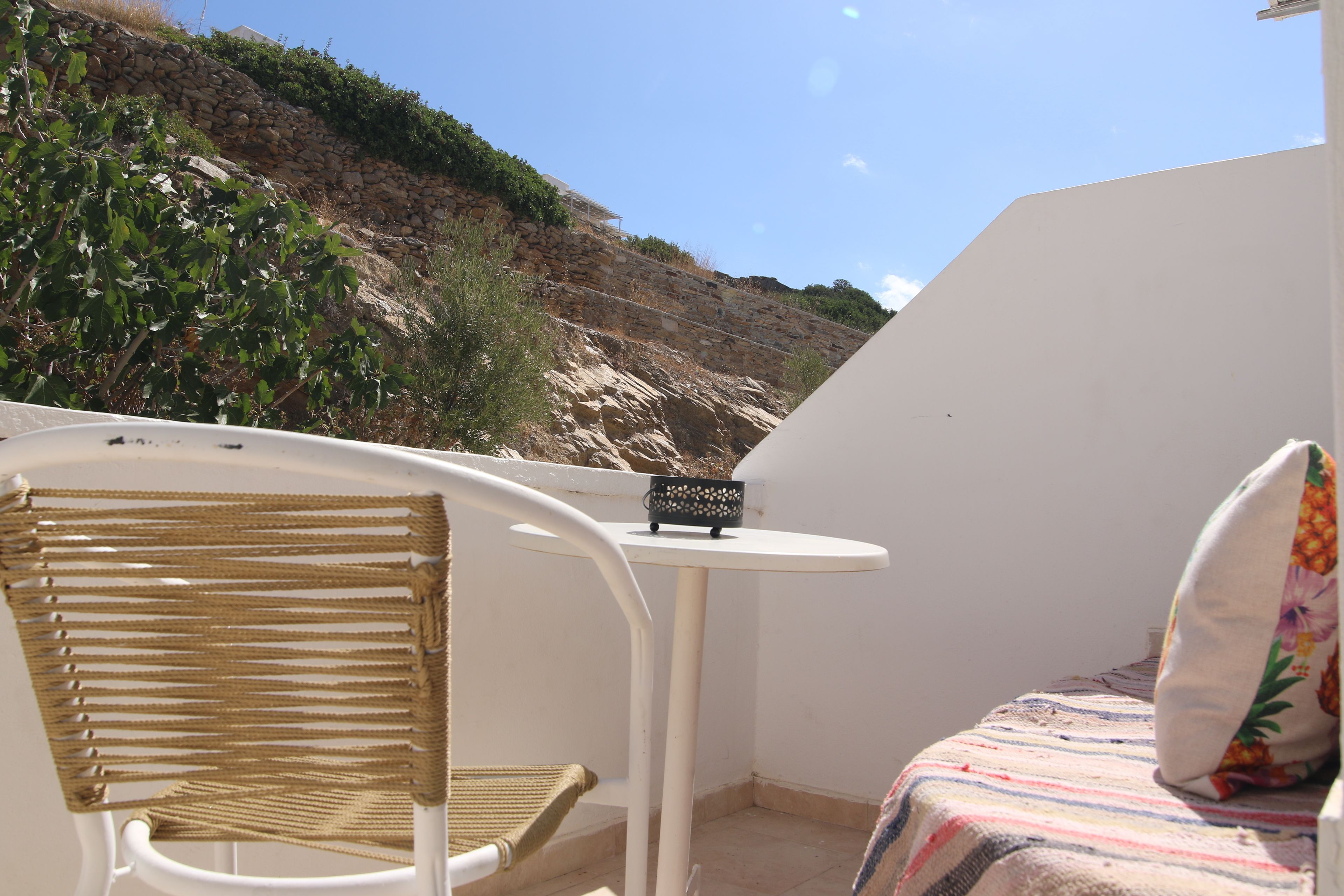 A balcony with a wicker chair, a small table, and a bed with a floral pillow.