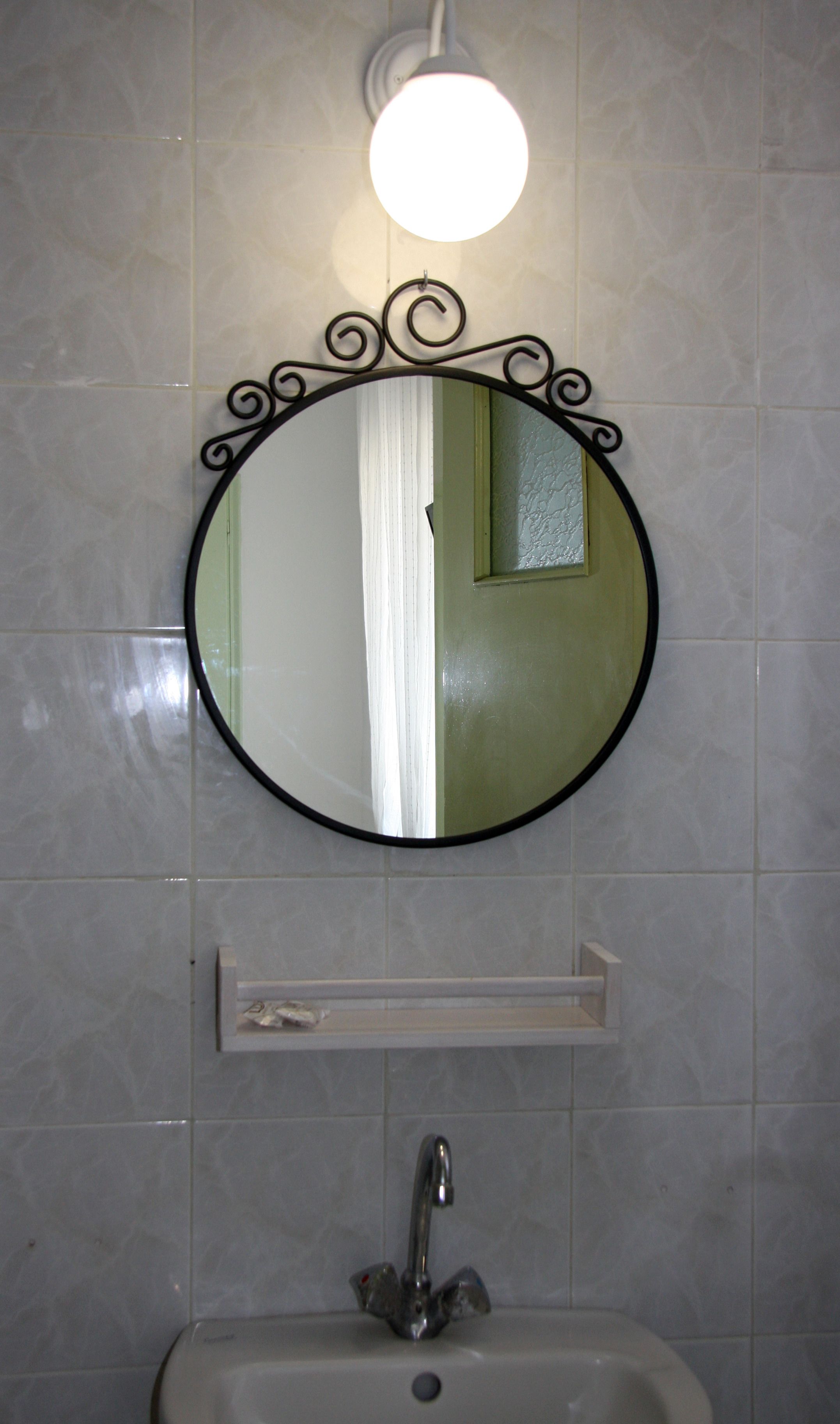 A bathroom with a round mirror, a light fixture above it, and a sink with a faucet.